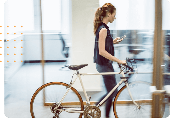 Woman walking her bicycle through an office while looking at her cell phone